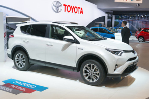 Brussels, Belgium - Januari 12, 2016: White Toyota Land RAV4 Hybrid crossover SUV front view. The Recreational Active Vehicle with 4-wheel drive hybrid version combines a 2.5-liter Atkinson cycle petrol engine with a powerful electric motor. The car is on display during the 2016 Brussels Motor Show. The car is displayed on a motor show stand, with lights reflecting off of the body. There are people looking around and other cars on display in the background.