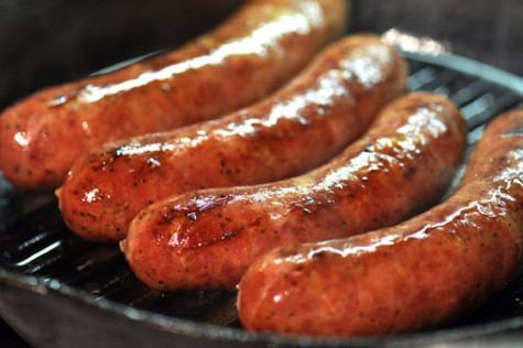 Four large sausages cooking in a cast iron skillet.