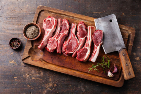 Raw fresh lamb ribs with pepper and cumin and meat cleaver on wooden cutting board on dark background