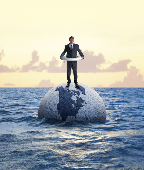 A businessman in a life preserver standing on a sinking globe in the middle of the ocean.