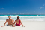 senior couple in bathing clothes relaxing on white sandy beach facing the ocean